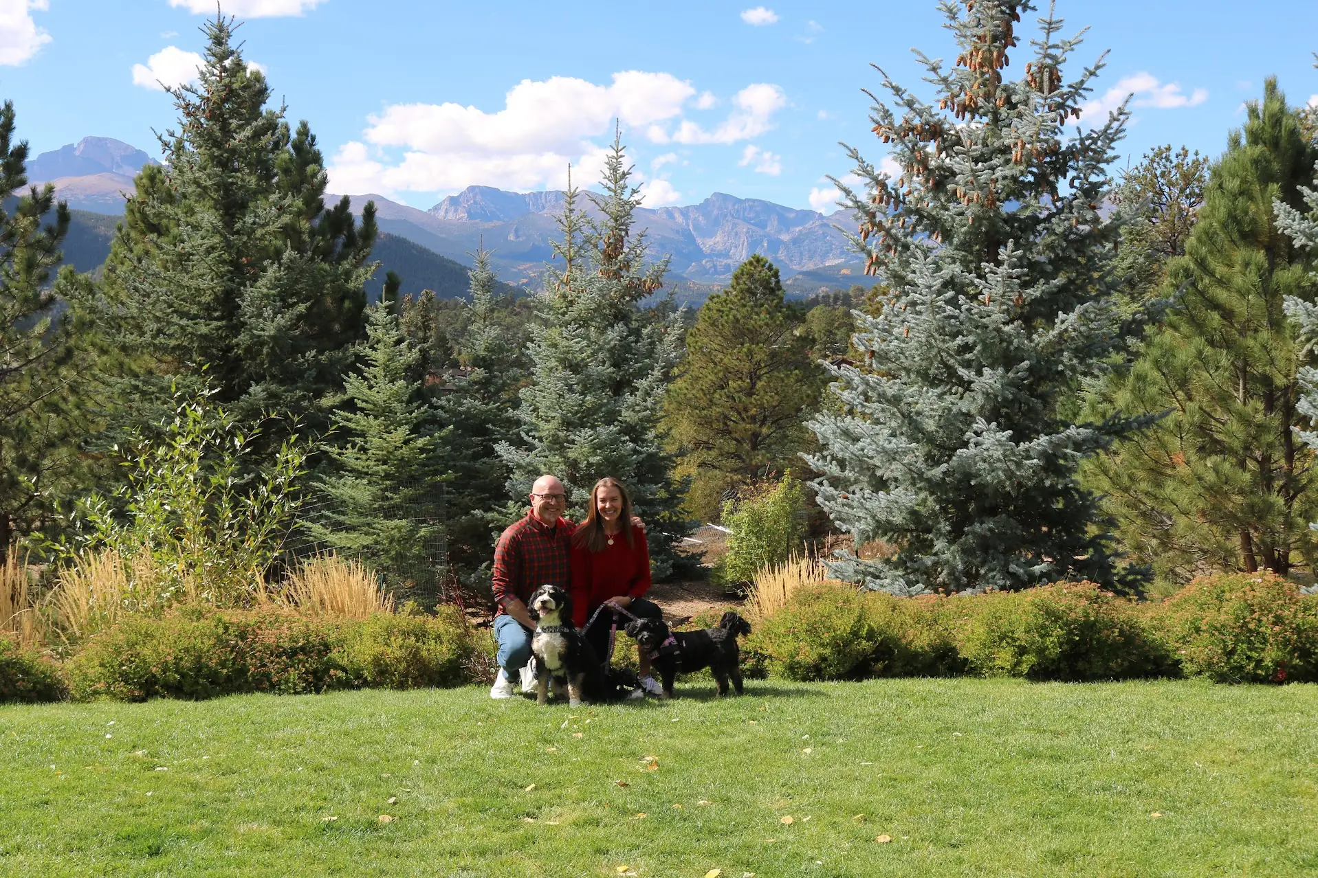 Mark and his family kneeling on a lawn with Bernie and Teddi, pine trees and the Rocky Mountains behind them