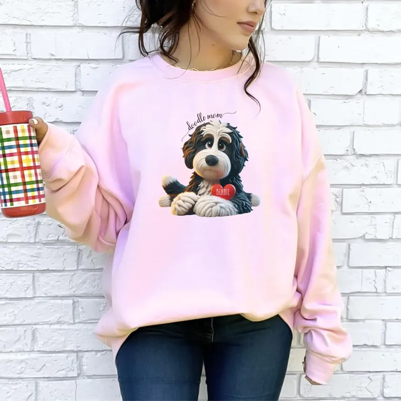 Pink sweatshirt with a clay-style Bernedoodle holding a red heart reading Bernie under the words doodle mom
